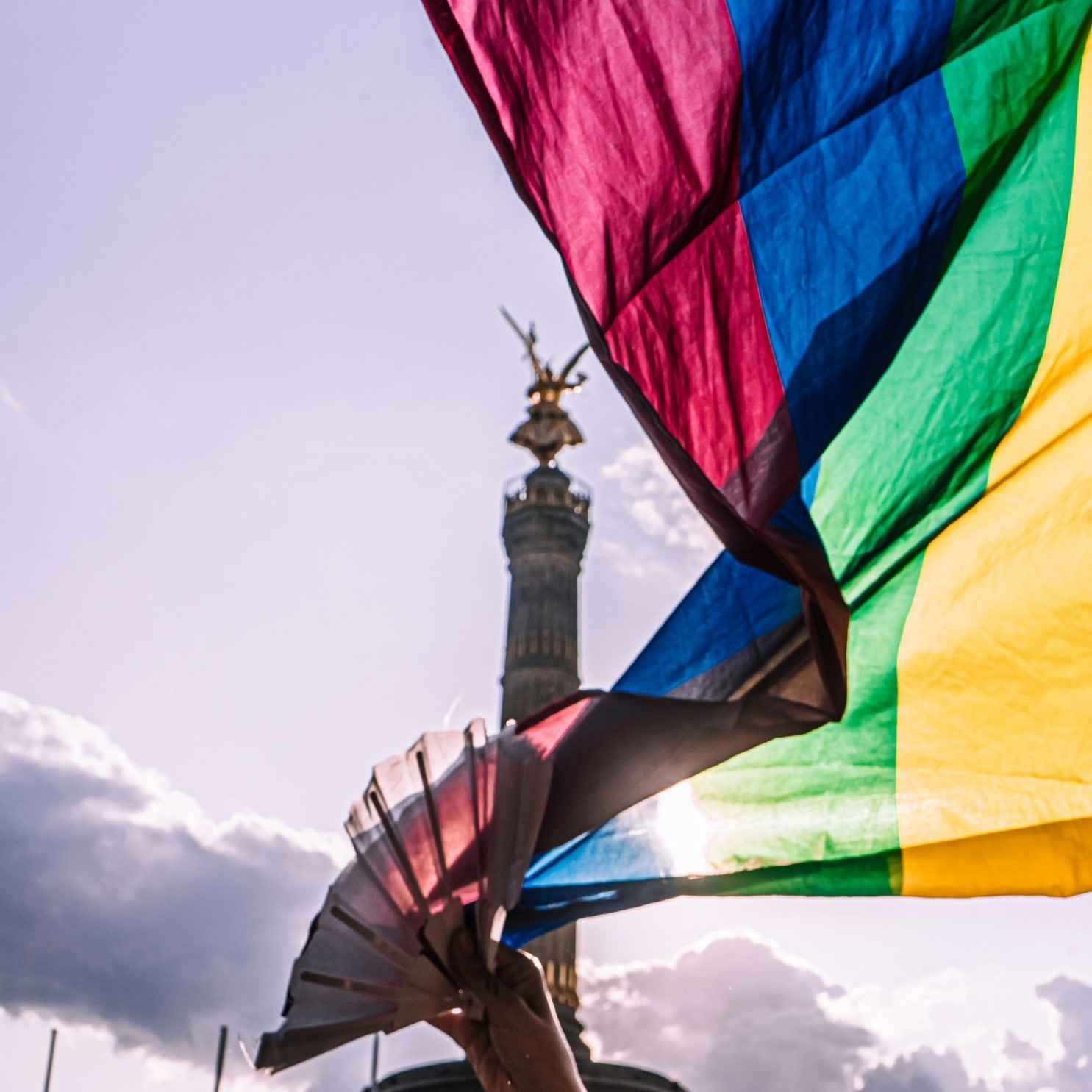 Auf dem Bild ist die Siegessäule zu sehen und davor eine Pride Flagge